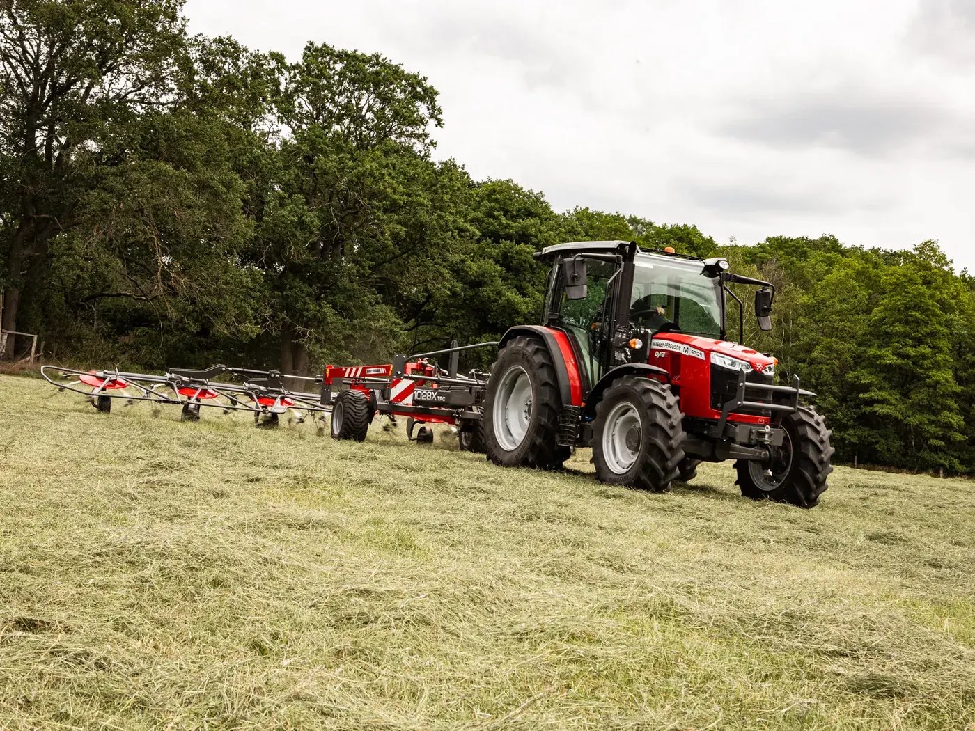Un tracteur Massey Ferguson 4709 M et sa faneuse dans un pré fauché