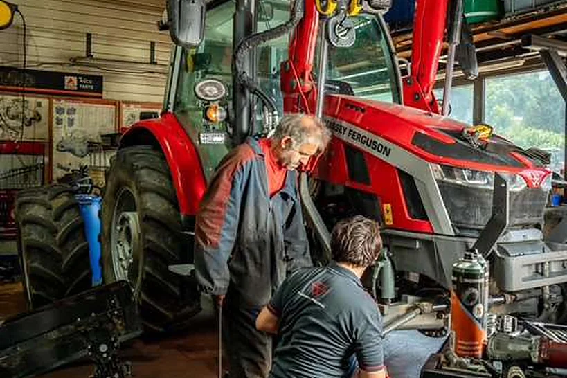 Deux techniciens au travail sous un tracteur Massey Ferguson, à l'atelier