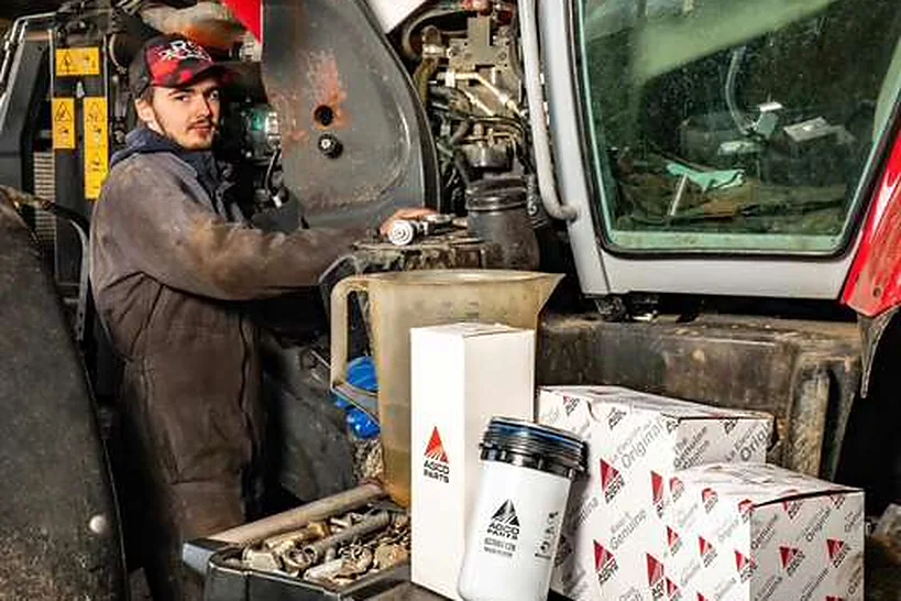 Un technicien dans le moteur d'un tracteur, cartons de pièces AGCO à côté